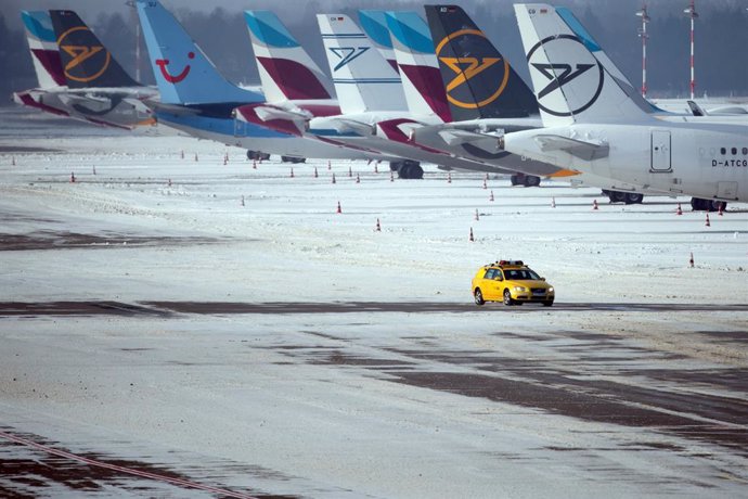 09 February 2021, North Rhine-Westphalia, Düsseldorf: An airport security vehicle drives across a snow-covered apron in Dusseldorf Airport next to parked aircraft. Photo: Federico Gambarini/dpa