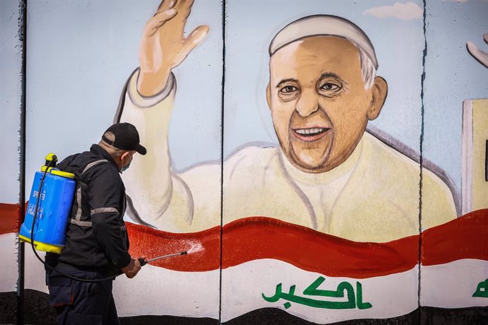 02 March 2021, Iraq, Baghdad: An Iraqi civil defense worker sprays disinfectant in front of a mural depicting Pope Francis in the Syriac Catholic Church of Our Lady of Salvation in Karrada district. Pope Francis is scheduled to visit Iraq from 05 to 08 
