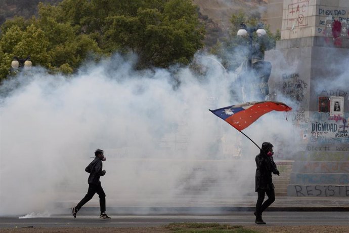 Dos manifestantes corren entre el humo de los botes lanzados por la Policía en una manifestación en Santiago de Chile.
