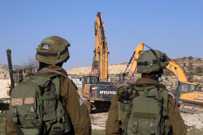 Soldados israelíes hacen guardia mientras las excavadoras se preparan para destruir una casa palestina en Cisjordania