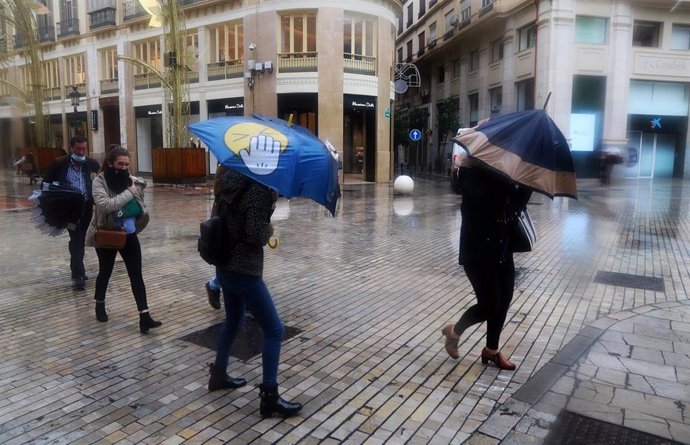 Archivo - Varias personas intentan resguardarse con el paraguas ante la lluvia y el viento