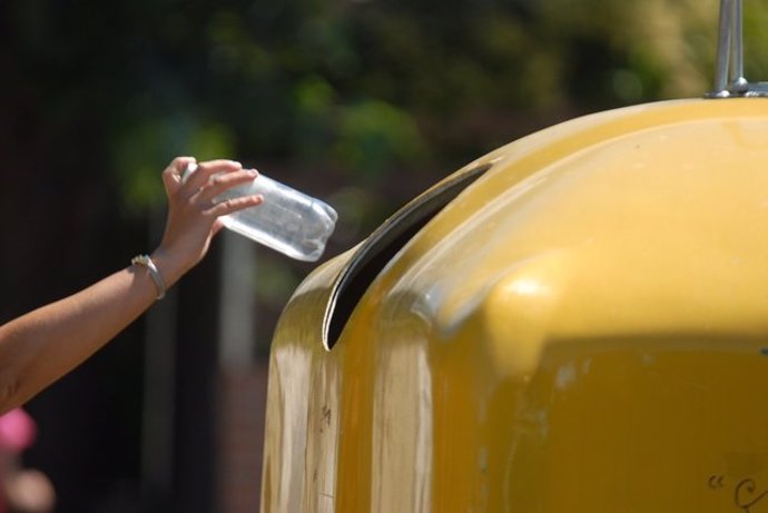 Una mujer tira un envase a un contenedor amarillo