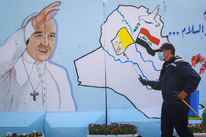 02 March 2021, Iraq, Baghdad: An Iraqi civil defense worker sprays disinfectant in front of a mural depicting Pope Francis in the Syriac Catholic Church of Our Lady of Salvation in Karrada district. Pope Francis is scheduled to visit Iraq from 05 to 08 