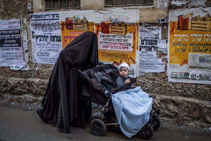 28 February 2021, Israel, Jerusalem: An Ultra Orthodox Jewish woman covered wearing a Haredi burqa pushes a baby stroller during the celebrations of the Jewish holiday of Purim at Jerusalem's Mea She'arim neighbourhood.  Purim, also called the Festival 