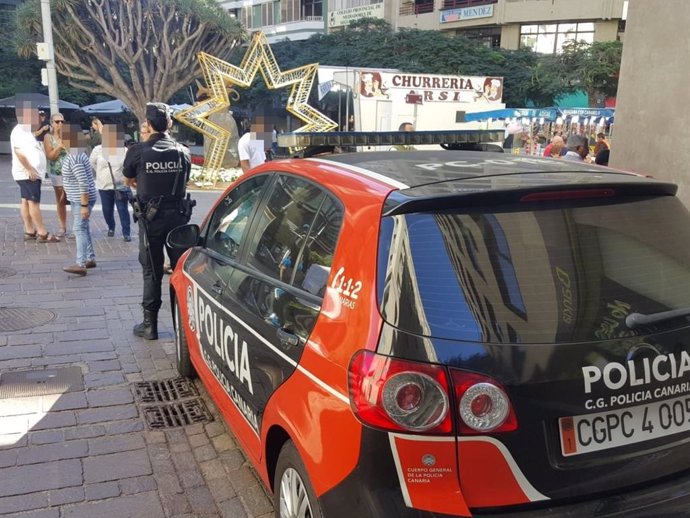 Archivo - Agente de la Policía Canaria junto a un coche patrulla