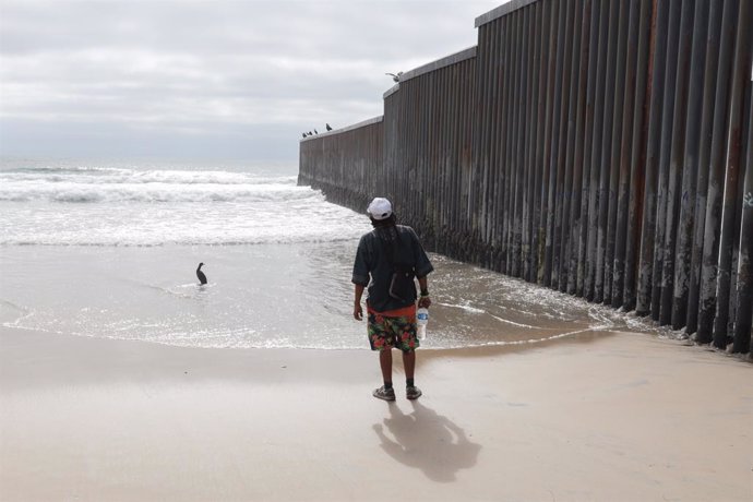 Archivo - Migrante en el muro de separación con EEUU