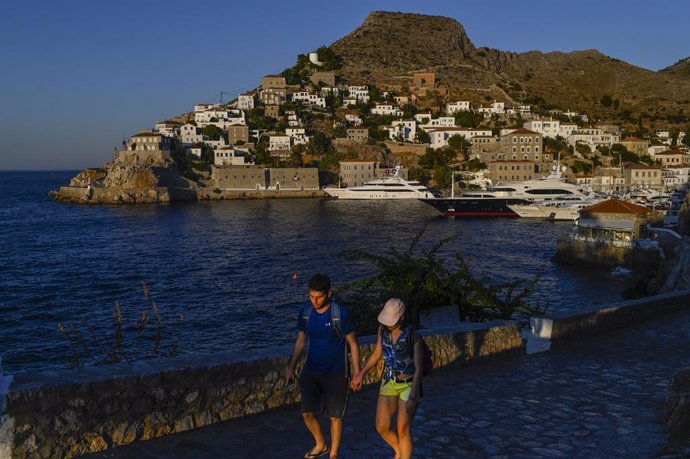 Archivo - 24 July 2020, Greece, Hydra: A couple hold hands as they walk past the harbour in the Greek island of Hydra. Cars, neon signs and plastic chairs are prohibited on Hydra island, which covers almost 50 square kilometres south-west of Athens. Pho
