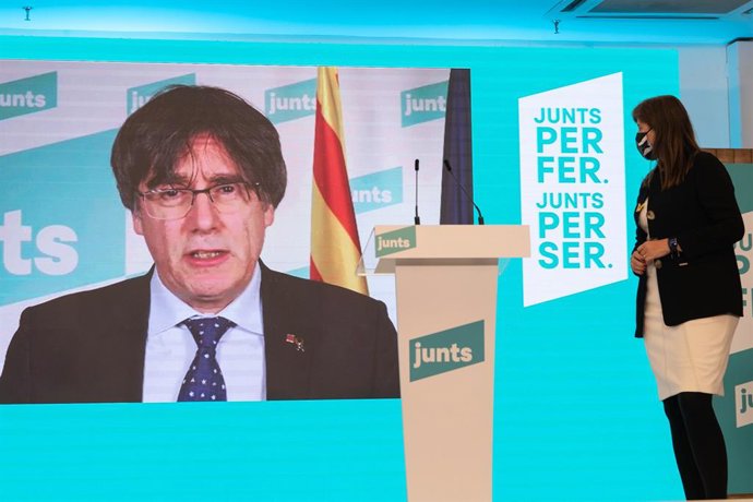 La número 2 de JxCat por Barcelona, Laura Borrás, observa al número 1 del partido por Barcelona, Carles Puigdemont (pantalla), durante una rueda de prensa para valorar los resultados obtenidos por su formación en los comicios catalanes durante la noche 