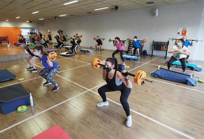 Un grupo de personas realiza deporte en la sala de un gimnasio. 