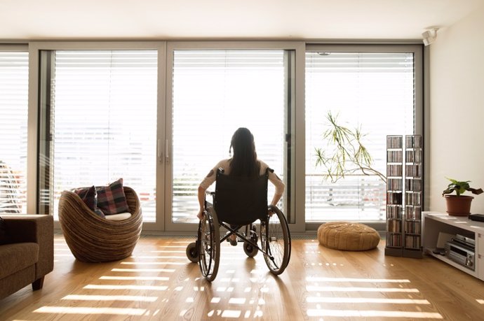 Archivo - Young disabled woman in wheelchair at home, rear view.