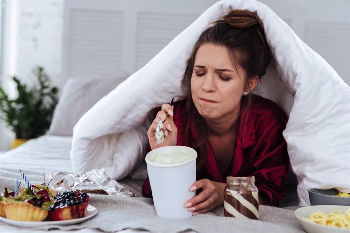 Archivo - Mujer comiendo con ansiedad en la cama.