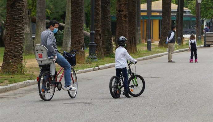 Archivo - Un padre paseando en bicicleta con su hijo en Sevilla.
