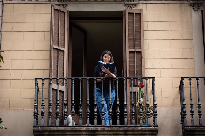 Archivo - Una joven lee un libro en el balcón de su casa (imagen de archivo)
