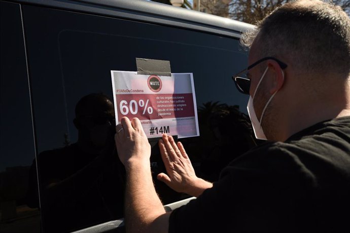 Un hombre pega una pancarta en un coche durante una caravana de vehículos por la reactivación de la cultura, en Valncia