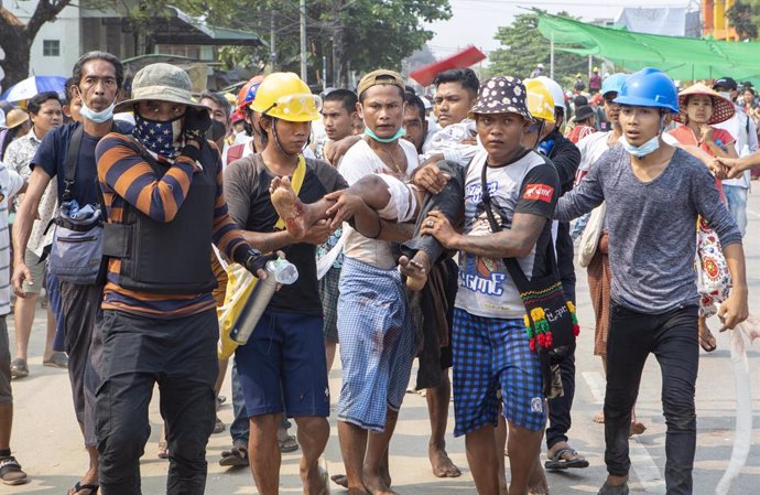 14 March 2021, Myanmar, Yangon: Protesters carry a protester who was shot in his leg by the police with live rounds during a protest against the military coup and the detention of civilian leaders. Five demonstrators have been killed in the latest crack