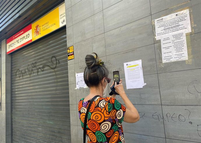 Archivo - Una mujer fotografía uno de los carteles con instrucciones para hacer trámites por internet colocados en la fachada de una oficina del SEPE.