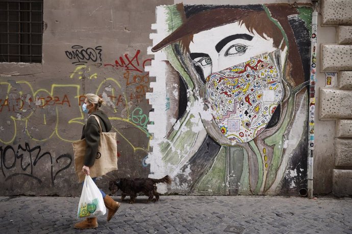 Una mujer con mascarilla pasea ante un mural en Roma