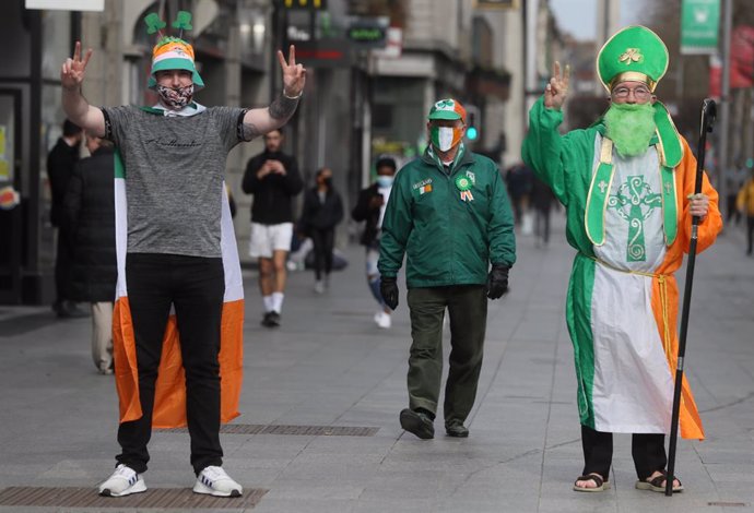 17 March 2021, Ireland, Dublin: Three men dressed up in the colours of the Irish national flag celebrate Saint Patrick's Day on O'Connell Street. Celebrations and parades for the annual St Patrick's Day event in Ireland are being held onlinefor the sec