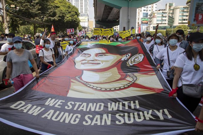 Manifestantes sujetan un cartel con una ilustración que representa a Aung San Suu Kyi.
