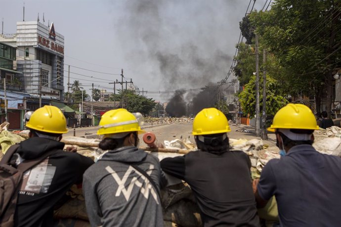 17 March 2021, Myanmar, Yangon: Demonstrators wearing yellow helmets watch armed soldiers and police during clashes at a demonstration against the military coup and the detention of civilian leaders. Photo: Thuya Zaw/ZUMA Wire/dpa