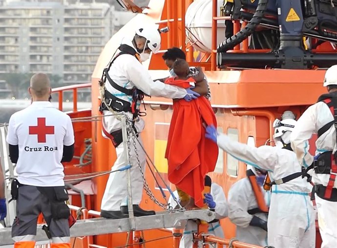 Un miembro de la Cruz Roja ayuda a bajar del barco a una mujer migrante con su niño en el puerto de Arguineguín 