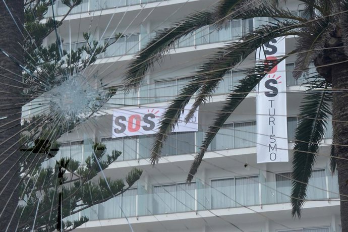 Archivo - Un cartel colgado de un edificio donde se puede leer "SOS Turismo", visto a través de un cristal roto.