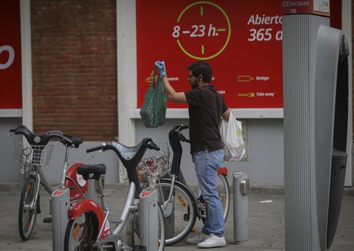 Archivo - Un hombre deposita una bolsa en una bicicleta del servicio Sevici 
