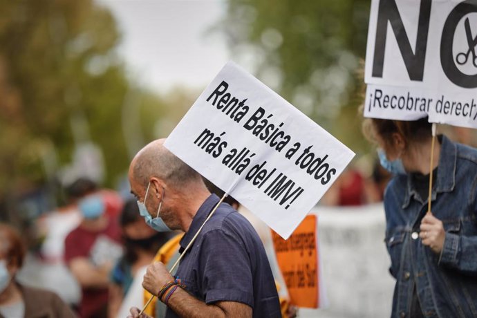 Archivo - Un hombre sostiene un cartel en el que se lee 'Renta Básica a todos más allá del IMV' durante una concentración en Madrid en octubre.