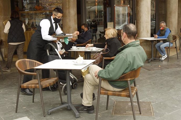 Un camarero atiende a varios clientes en la terraza de un bar.