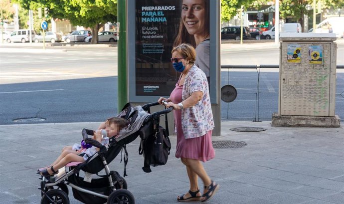 Archivo - Una señora con mascarillas pasea a dos niños ante un cartel publicitario en el primer día  de uso obligatorio de mascarillas en Sevilla a 15 de julio del 2020