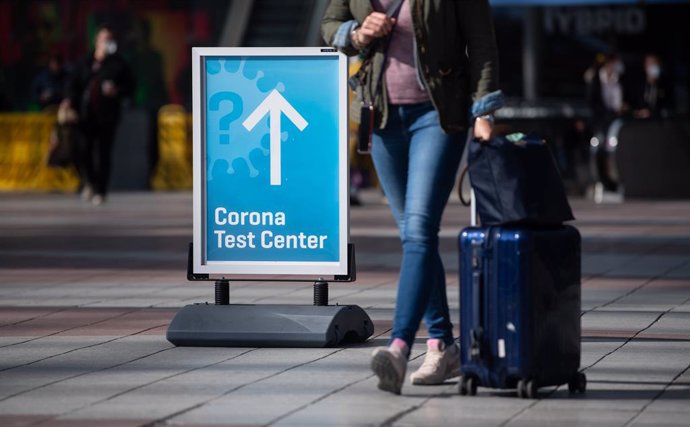 26 March 2021, Bavaria, Munich: A woman passes past a sign with the inscription "Corona Test Center" at Munich airport as Germany will require Covid-19 tests on flight arrivals starting from Sunday. Photo: Sven Hoppe/dpa