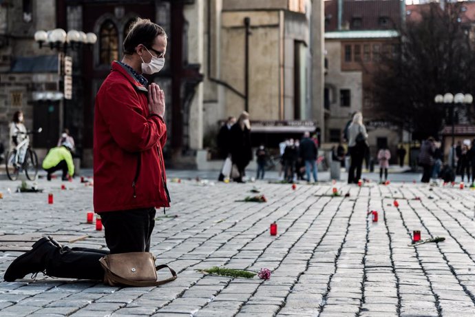 26 March 2021, Czech Republic, Prague: A man kneels on the ground to offer prayers along the slabs lining Prague's Old Town Square, which has been decorated with crosses in remembrance of those who died after contracting coronavirus. Photo: Tomas Tkacik