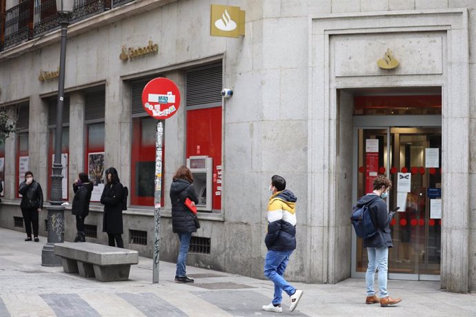 Archivo - Varias personas esperan en una cola respectando la distancia de seguridad para entrar en una sucursal del Banco Santander en Madrid.