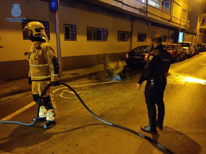 Un agente de la Policía Nacional y un bombero, junto a la motocicleta quemada.