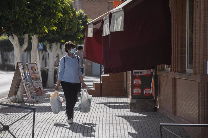 Archivo - Una mujer con bolsas de la compra pasea por una calle del municipio de La Algaba (Sevilla). Imagen de archivo.