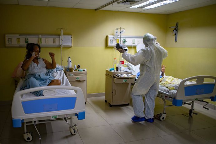 25 March 2021, Venezuela, Caracas: A health worker greets Covid-19 patients while using a small loudspeaker playing and music to try to raise good spirits in the ICU ward. Photo: Rafael Hernandez/dpa