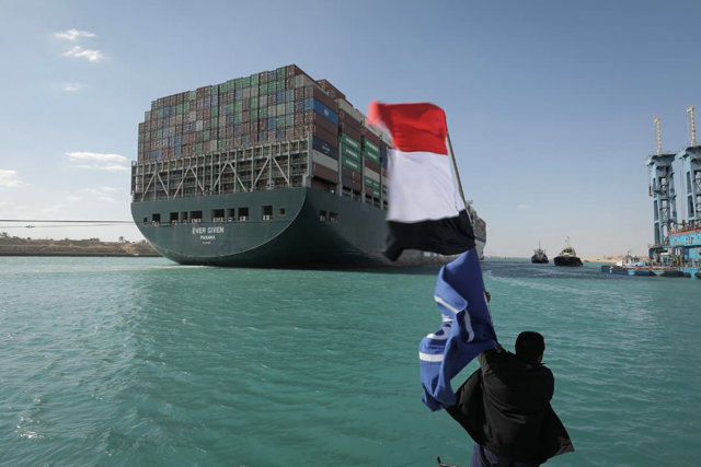 29 March 2021, Egypt, Suez: A worker waves the Egyptian flag as the "Ever Given" container ship operated by the Evergreen Marine Corporation, sails with tugboats through the Suez Canal.