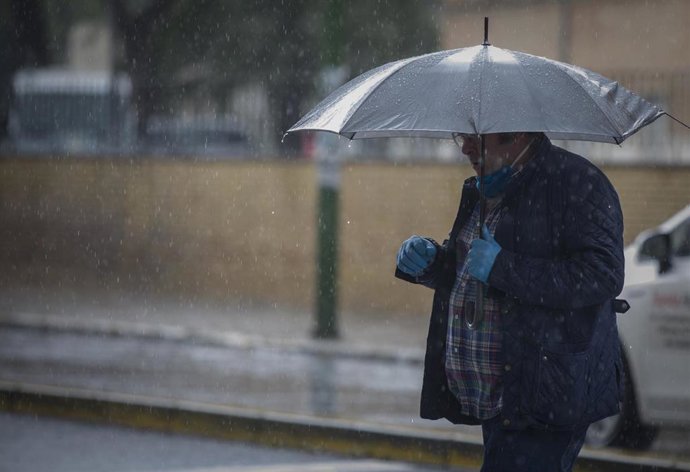 Archivo - Un hombre camina bajo la lluvia protegido con un paraguas, durante la alerta amarilla. En el estado de alarma por la crisis del coronavirus, (Covid-19). En Sevilla, (Andalucía, España), a 27 de abril de 2020.