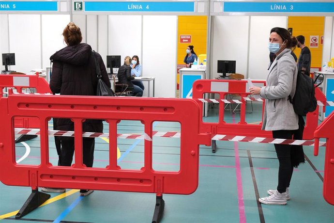 Varias personas realizan cola para que les suministren la vacuna contra la Covid-19 en el dispositivo de vacunación puesto en marcha en el polideportivo Germans Escalas.