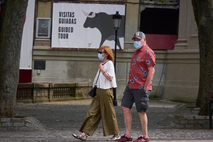 Archivo - Dos turistas pasean delante de un cartel en la plaza de toros de Pamplona.