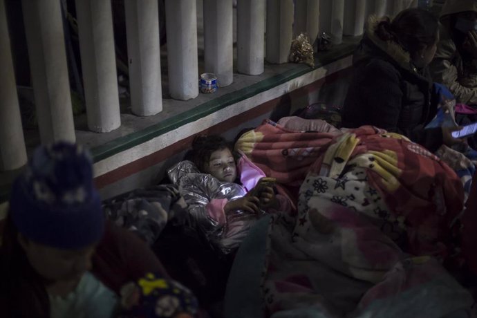 Archivo - Una niña mira un celular mientras duerme en la explanada del Instituto Nacional de Migración cerca del paso fronterizo El Chaparral, entre migrantes centroamericanos y mexicanos.