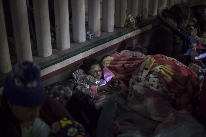 Archivo - 19 February 2021, Mexico, Tijuana: A girl looks at a cell phone while sleeping on the esplanade of the National Institute of Migration near the El Chaparral border crossing, among Central American and Mexican migrants waiting for US authoritie