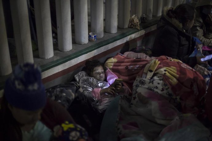 Archivo - 19 February 2021, Mexico, Tijuana: A girl looks at a cell phone while sleeping on the esplanade of the National Institute of Migration near the El Chaparral border crossing, among Central American and Mexican migrants waiting for US authoritie