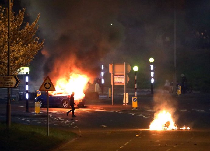 03 April 2021, United Kingdom, Belfast: A man walks past a burning car after violence broke out in Newtownabbey. Photo: Peter Morrison/PA Wire/dpa
