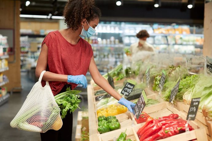 Mujer comprando verduras con mascarilla y guantes en un supermercado.