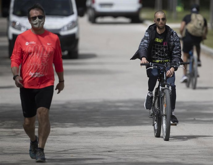 Un hombre circula bicicleta, sin mascarilla, por un parque.