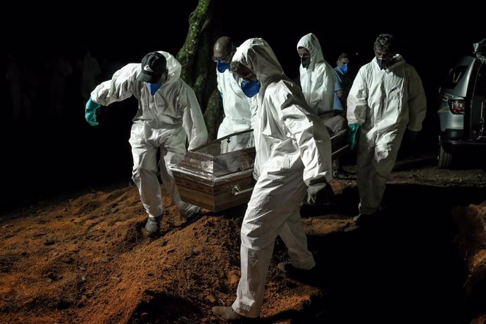 02 April 2021, Brazil, Sao Paulo: Employees of the Vila Formosa cemetery, the largest in Latin America, carry a coffin to bury a person who died of coronavirus (Covid-19). Due to the high number of deaths, the employees also work during the night. Photo