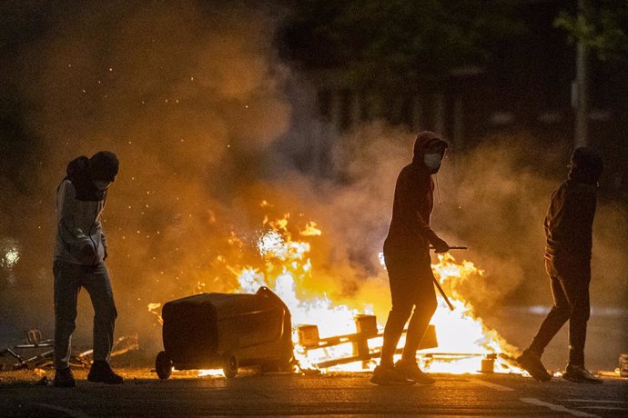 07 April 2021, United Kingdom, Belfast: People stand next to a fire during further unrest. Northern Ireland has had several consecutive nights of street violence and disorder in a number of mainly loyalist areas following a controversial decision last w
