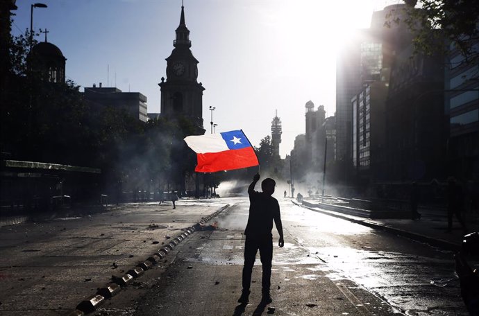 Archivo - 29 October 2019, Chile, Santiago: A demonstrator waves a Chilean flag during clashes following an anti-government protest. For the past two weeks, Chile has been experiencing a wave of strong protests that led to the replacement of eight minis