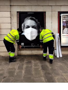 Dos operarios pegan un cartel de la campaña de apoyo a los sanitarios 'Behind de Mask', en una fotografía del 6 de abril del 2021.